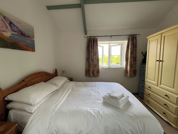A bedroom with a bed, a window with curtains, a wardrobe, and a painting on the wall.