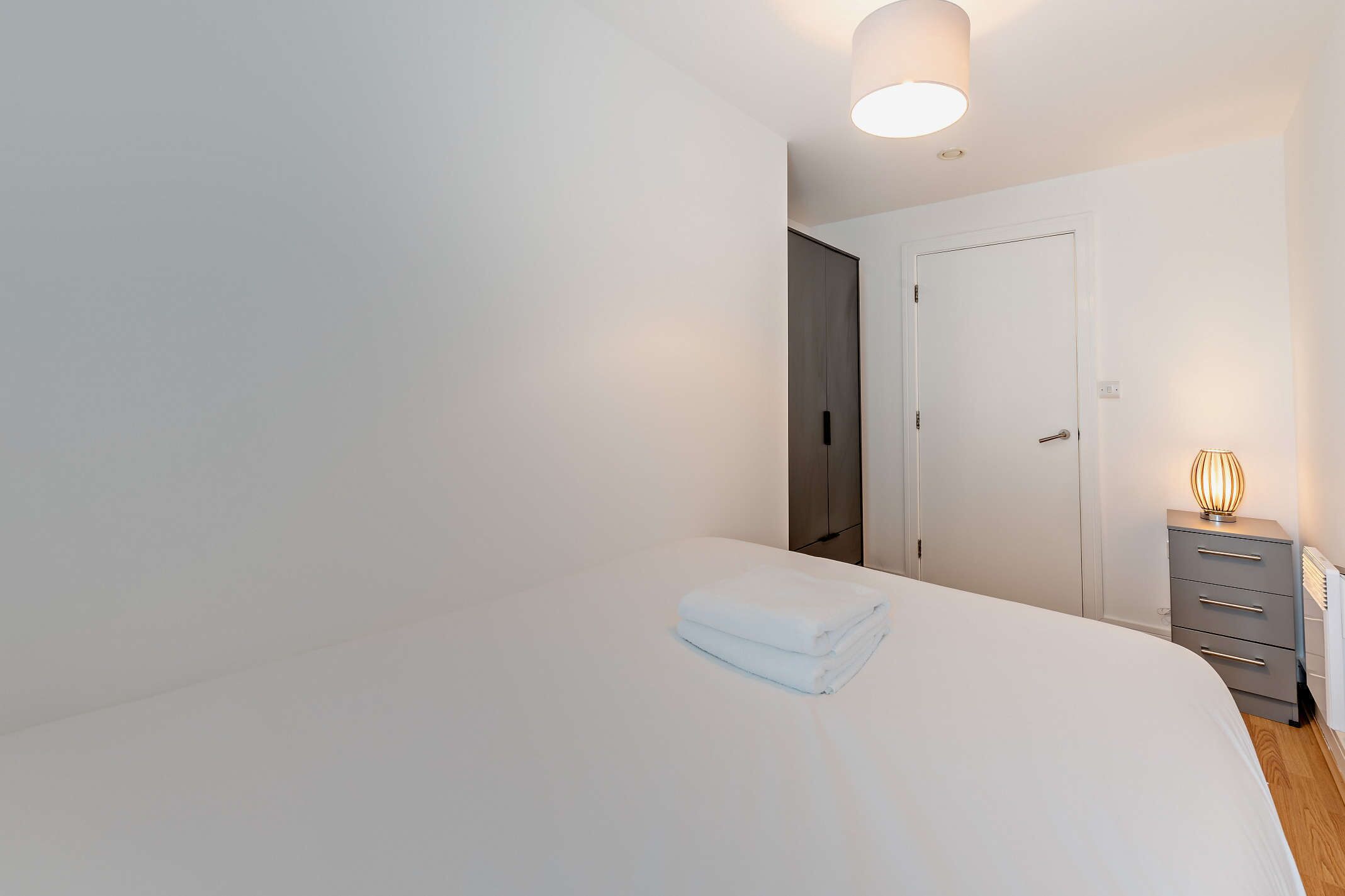 A bedroom with a bed, a bedside table with a lamp, and a wardrobe.