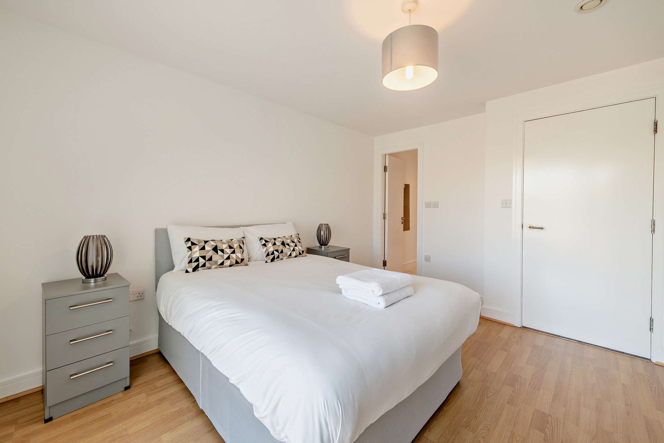 A bedroom with a bed, bedside tables, a wardrobe, and a hanging light fixture.