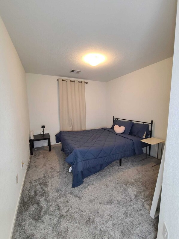 A bedroom with a bed, a nightstand, a lamp, and a window with curtains. - Family-Friendly Houston Home (Houston)