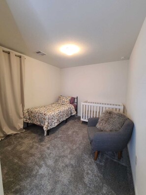 A bedroom with a bed, a crib, a chair, and a curtain. - Family-Friendly Houston Home (Houston)
