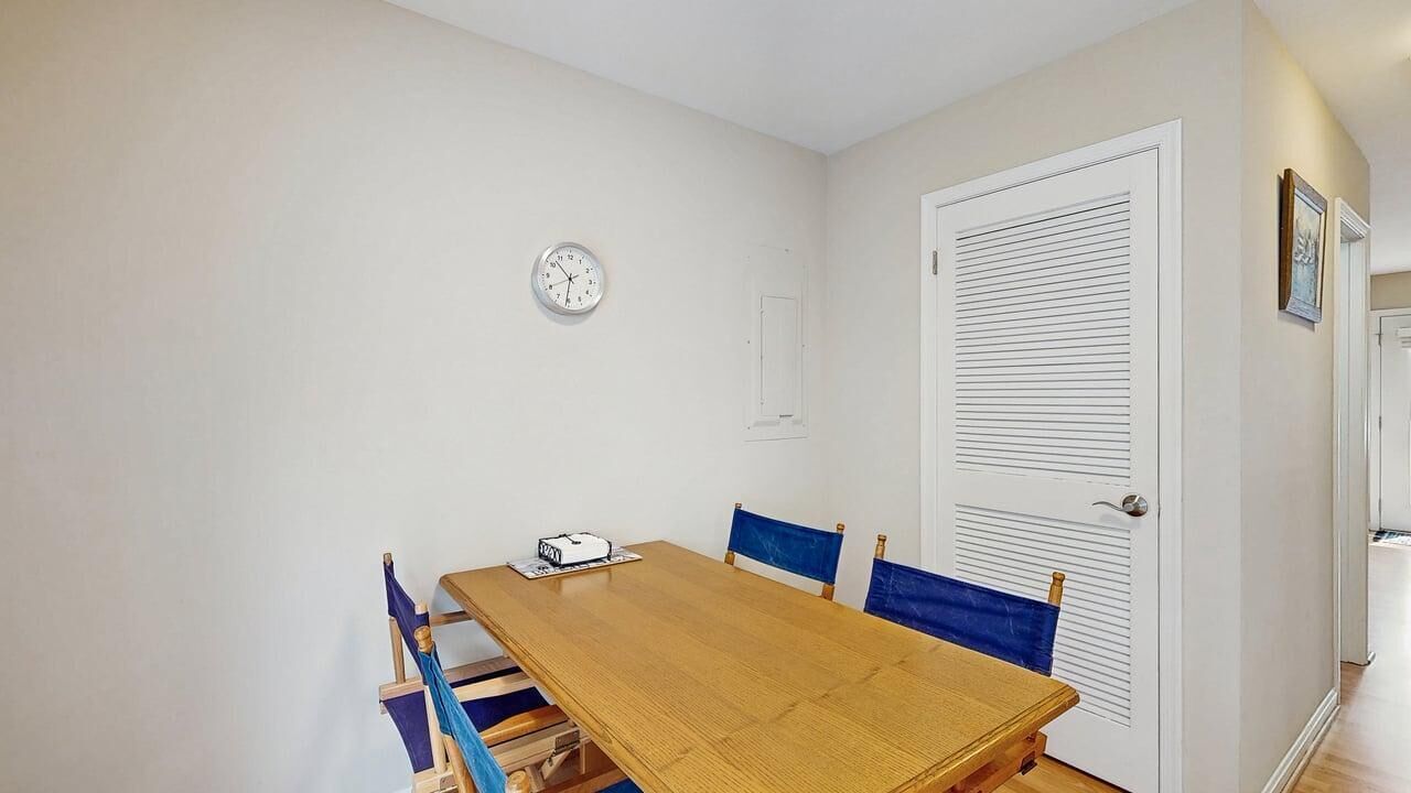 Une pièce avec une table en bois, des chaises bleues, une porte blanche dotée de panneaux à persiennes horizontales et une horloge murale.