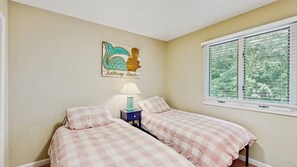 Une chambre avec deux lits, une table de chevet avec une lampe, une fenêtre avec des stores et un élément décoratif mural.