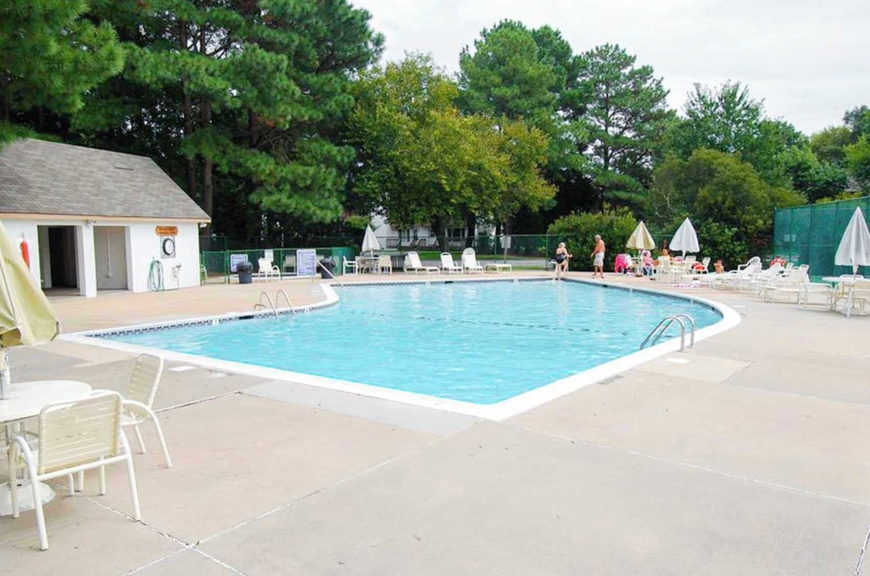 A swimming pool with lounge chairs and umbrellas, surrounded by trees.