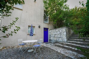 A courtyard with a table and chairs, a blue door, and stone steps leading up to a building.