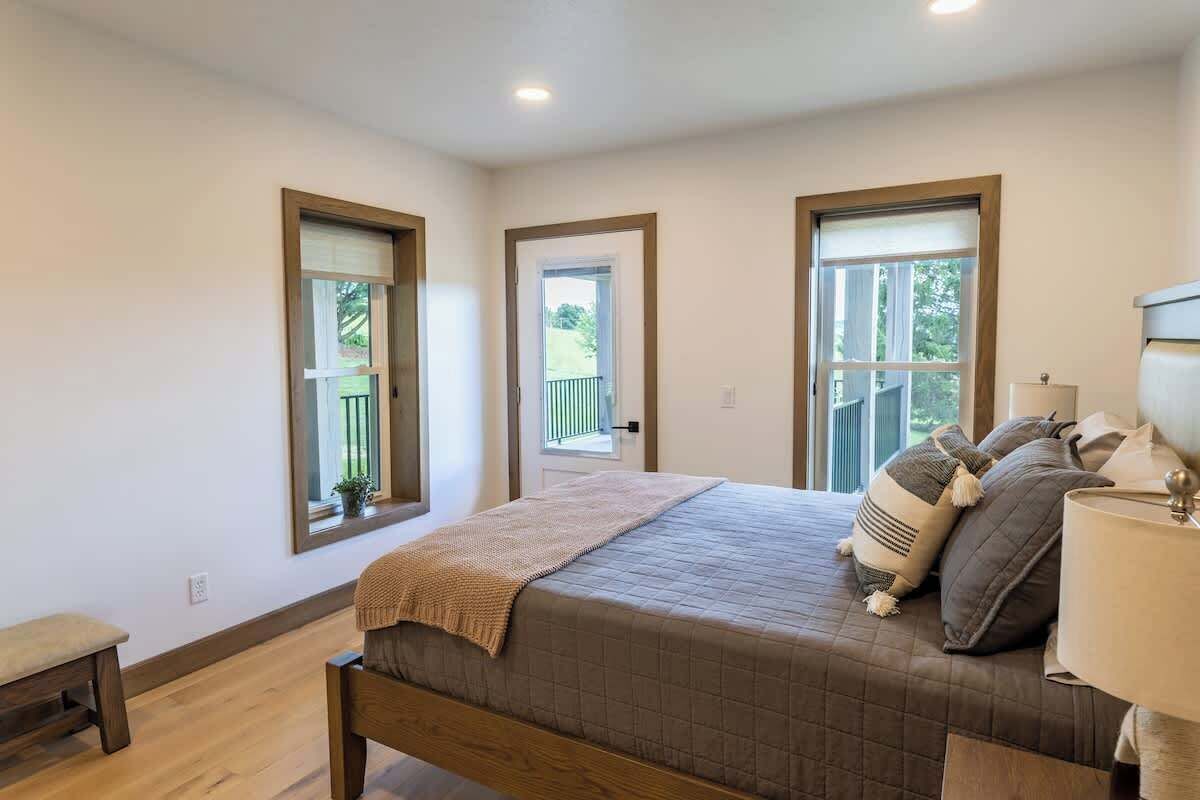 A bedroom with a bed, a bench, a lamp, and three windows.