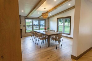 Zona pranzo con tavolo e sedie in legno, ampie finestre e lampadario.