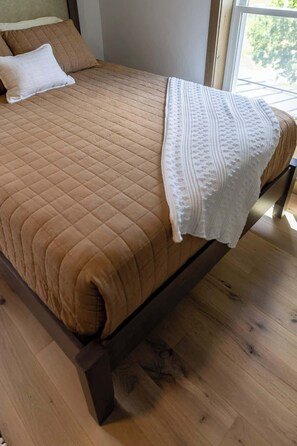 Un letto con una coperta trapuntata marrone e una coperta bianca con motivo a rilievo.