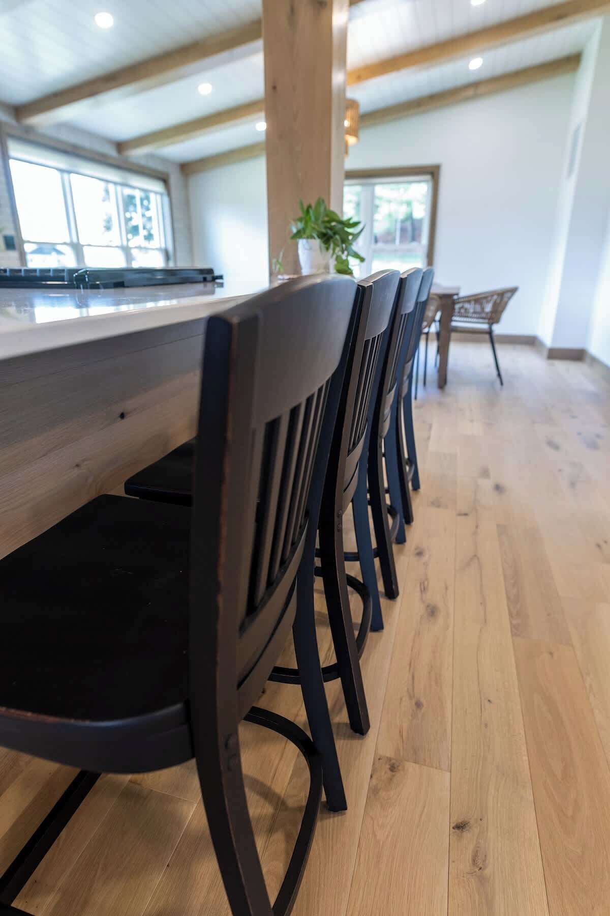 A modern kitchen with a long counter and black chairs.