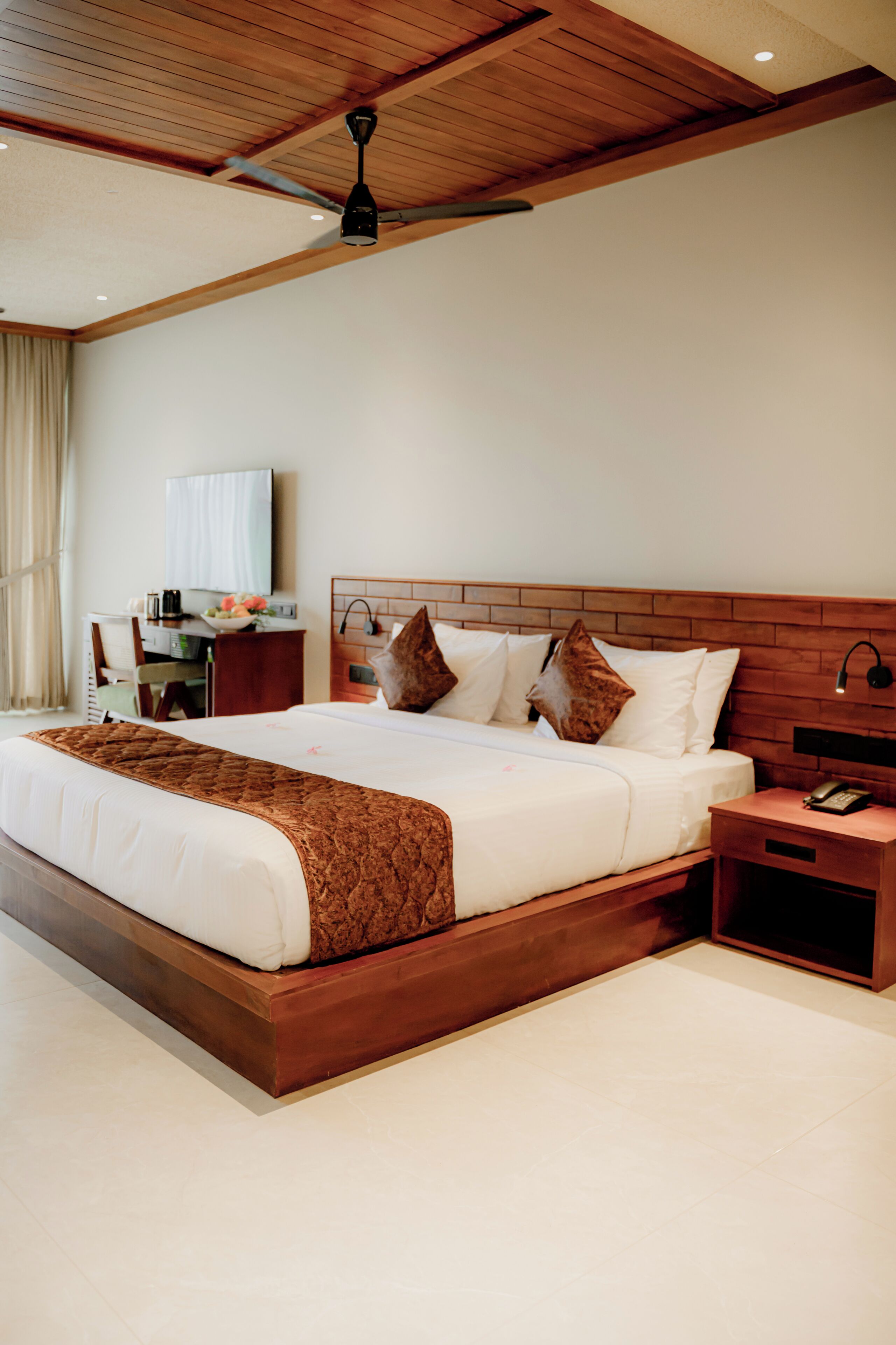 A hotel room with a large bed, wooden headboard, bedside tables, a desk, and a ceiling fan.