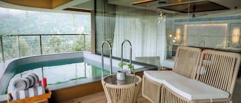 A modern balcony with a pool, wicker furniture, and a view of greenery.