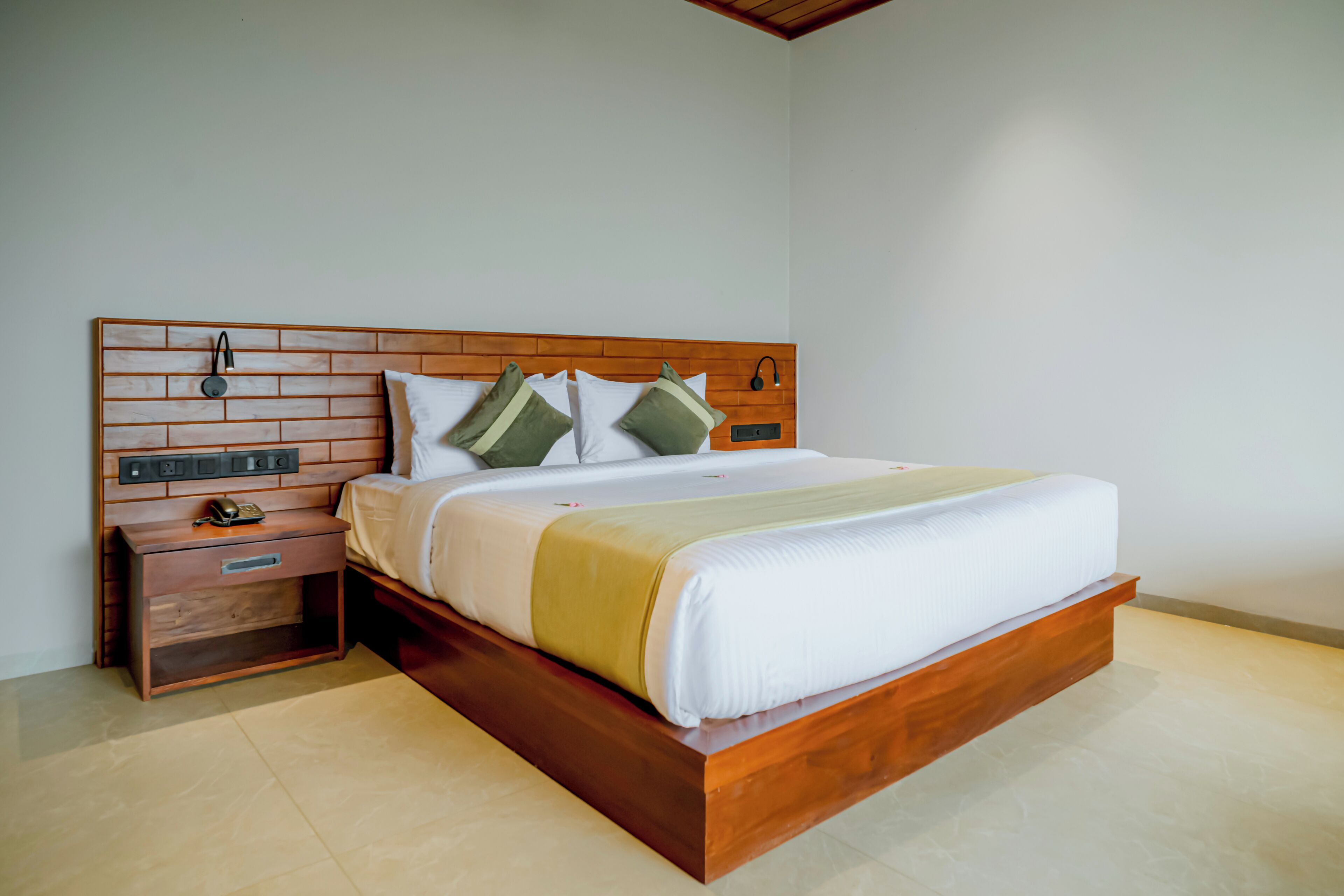A bedroom with a wooden headboard, a bed with white bedding, a nightstand with a phone, and a bedside table.