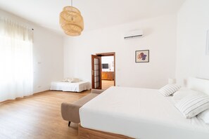 A bedroom with a large bed, a sofa, a hanging light fixture, and a door leading to another room. - Appartamento in Piazzetta by Wonderful Italy (Naples)