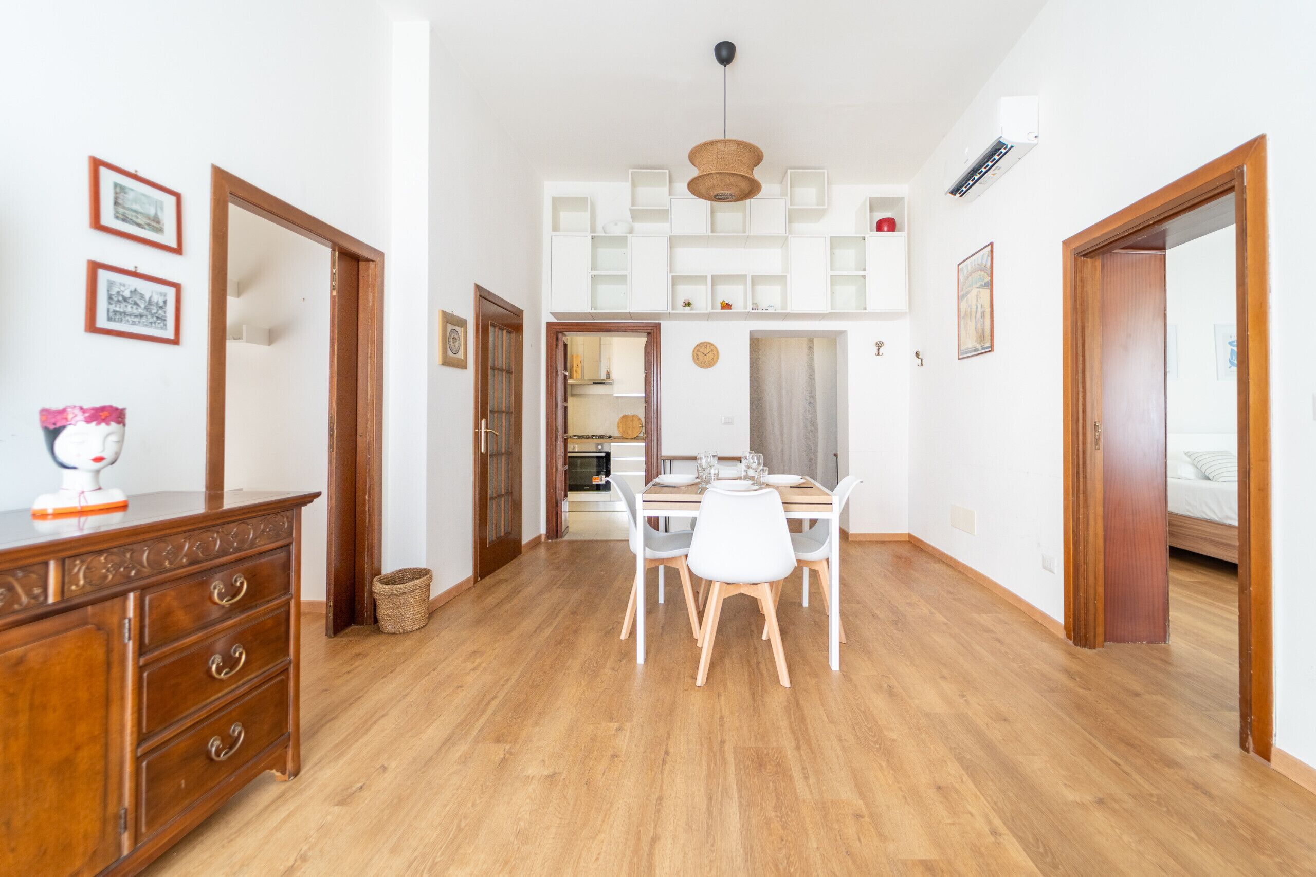 A spacious room with a wooden floor, a dining table with chairs, a kitchen area, and a staircase leading to an upper level.