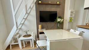 Ein kompakter Wohnraum mit Treppe, einem an der Wand befestigten Flachbildfernseher, einer kleinen Essecke und einer Küchenzeile.