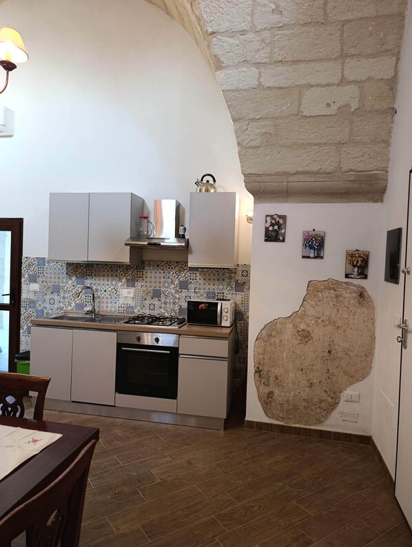 Cocina con gabinetes blancos, microondas, tetera y salpicadero de azulejos.