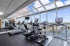 A gym with treadmills and exercise equipment, large windows, and a view of a body of water.