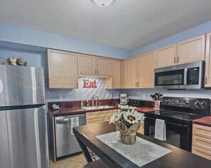 A kitchen with wooden cabinets, a stainless steel refrigerator, a microwave, and a stove.