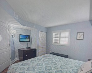 A bedroom with a bed, a dresser, a television, and a window.