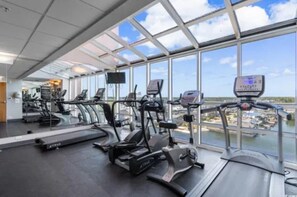 A gym with treadmills, stationary bikes, and elliptical machines, featuring large windows and a view of the city. - Ocean View| King Bed | Pools & Lazy River |CG Pier (North Myrtle Beach)