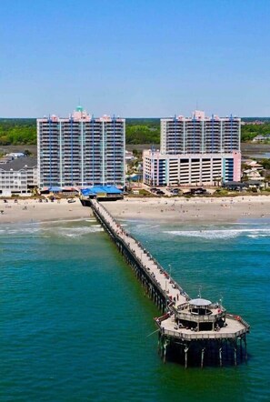 A pier extending into the water with a beach and two large hotels in the background. - Prince Resort |Ocean View| King Bed | Pools & Lazy River (North Myrtle Beach)