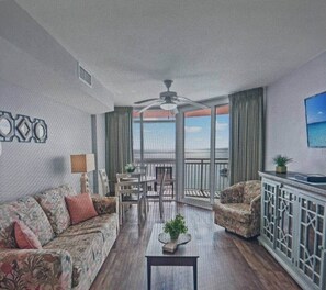 A living room with a sofa, armchair, coffee table, and a balcony with a view.