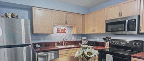 Une cuisine moderne avec des meubles en bois, des appareils électroménagers en acier inoxydable et un îlot central agrémenté d’un vase de fleurs.