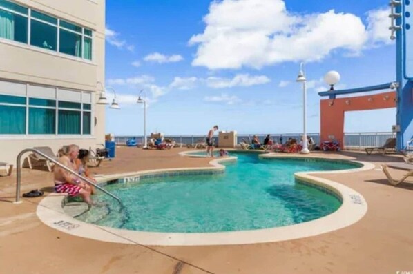 A pool area with multiple swimming pools, lounge chairs, and a building with large windows.