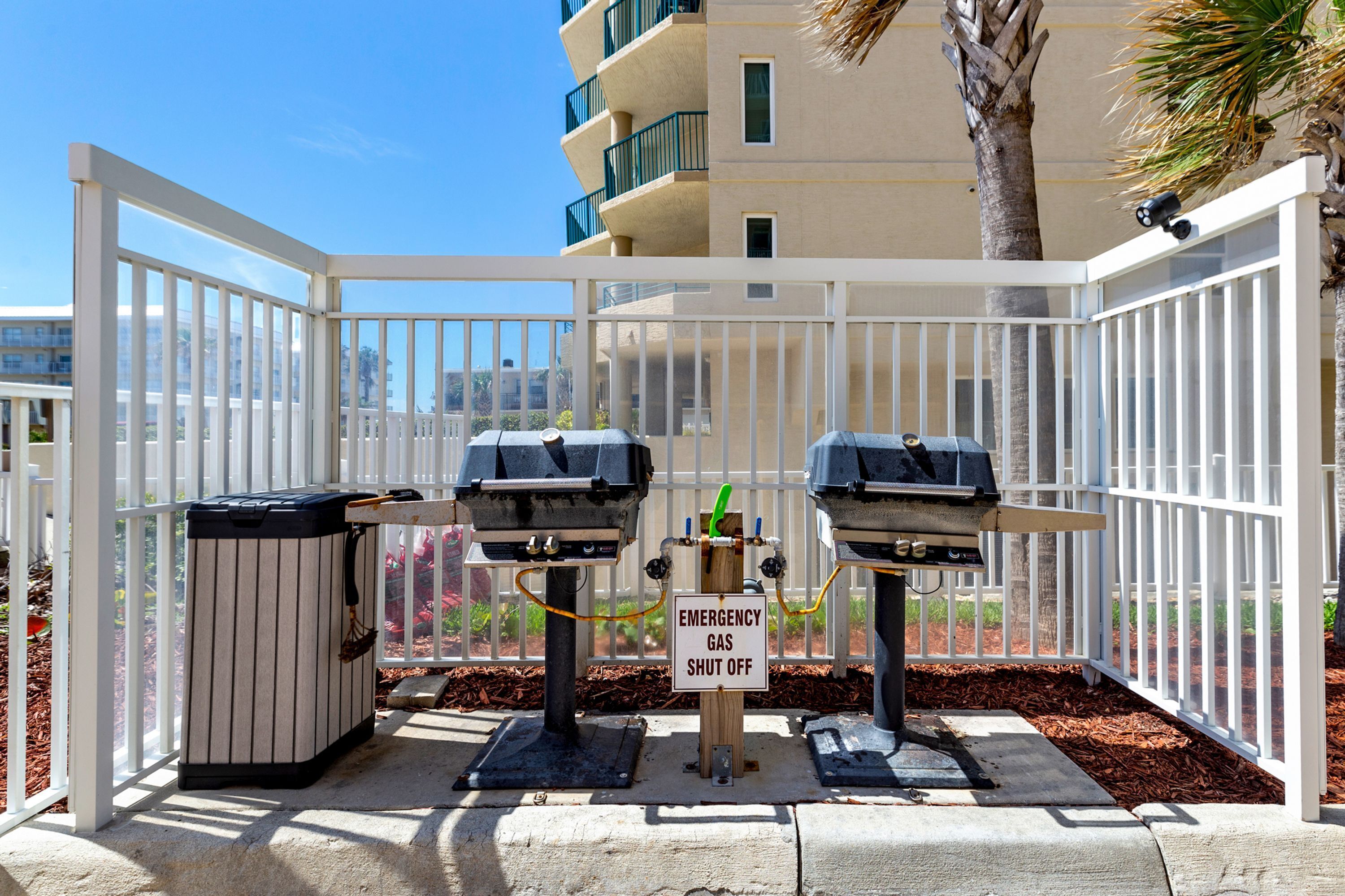 Un espace barbecue équipé de deux grils, d’une poubelle et d’un panneau indiquant l’emplacement de la vanne d’arrêt d’urgence du gaz.