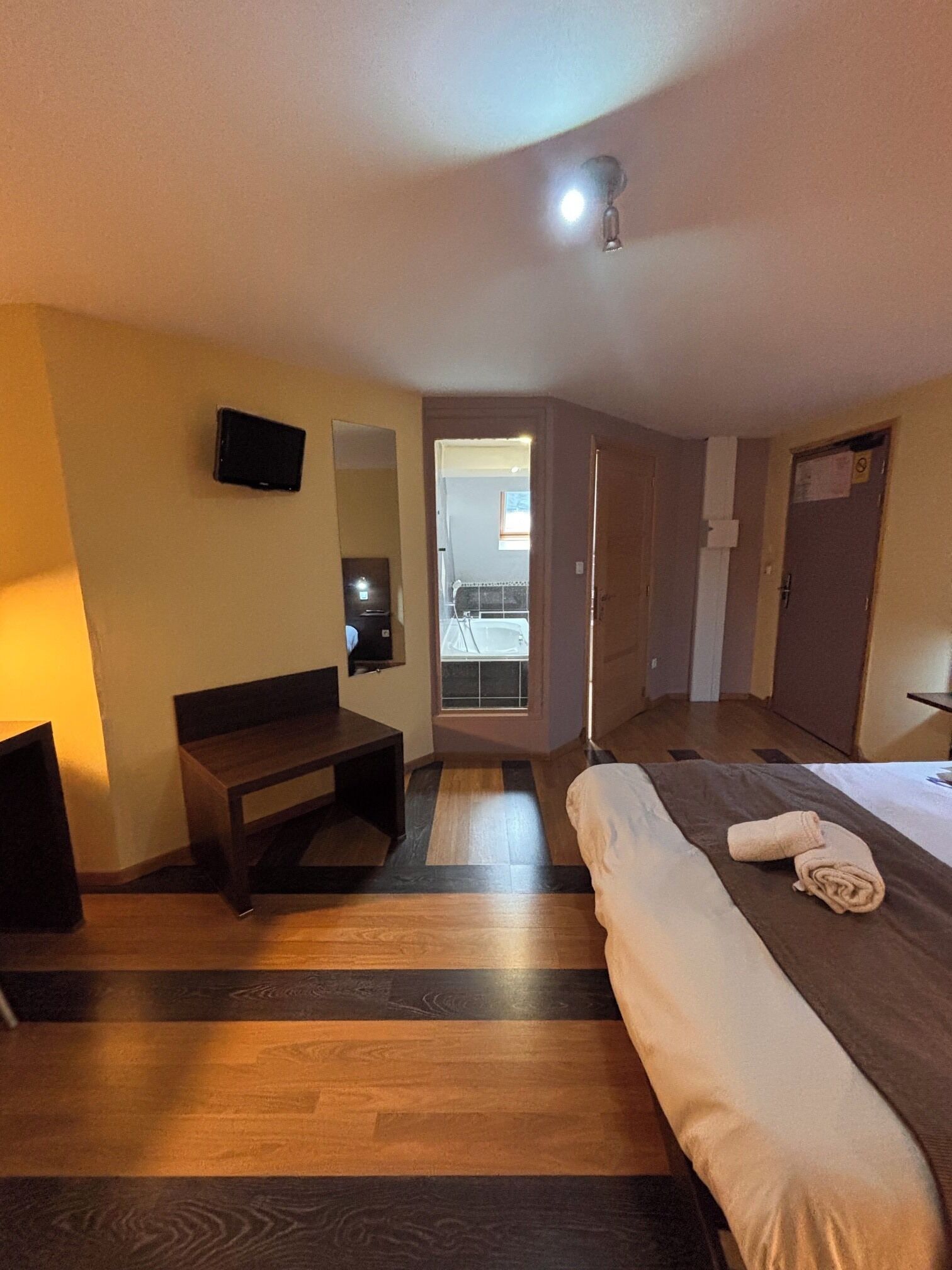 Une chambre d’hôtel avec un lit, un bureau, une chaise, une télévision et une salle de bain visible à travers une porte ouverte.