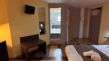 Une chambre d’hôtel avec un lit, un bureau, une chaise, une télévision et une salle de bain visible à travers une porte ouverte.