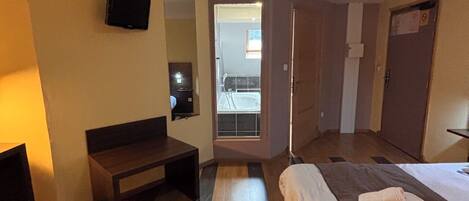 A hotel room with a bed, a desk, a chair, a television, and a bathroom visible through an open door.