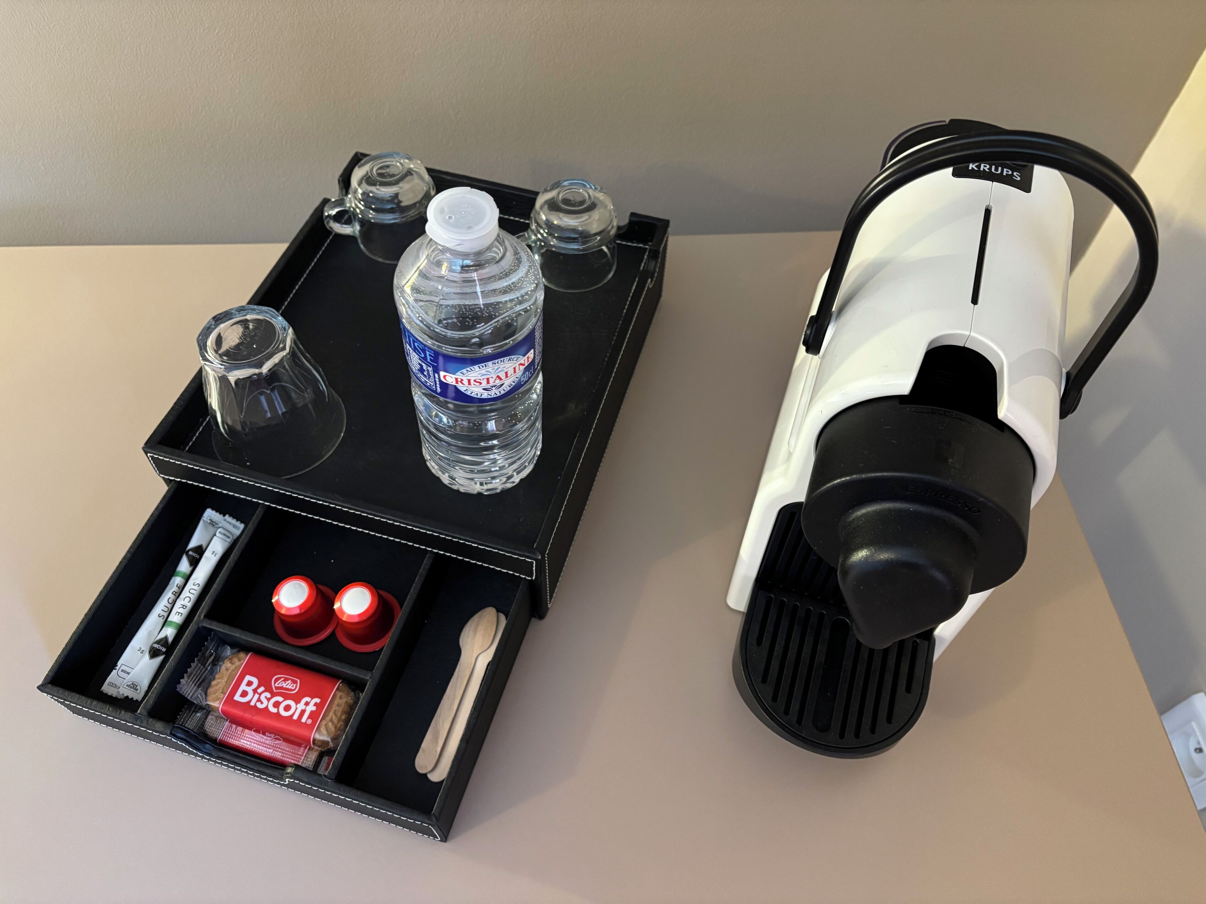 A black tray with a bottle of water, two glasses, a toothbrush, a tube of toothpaste, a red box of biscuits, and a spoon.