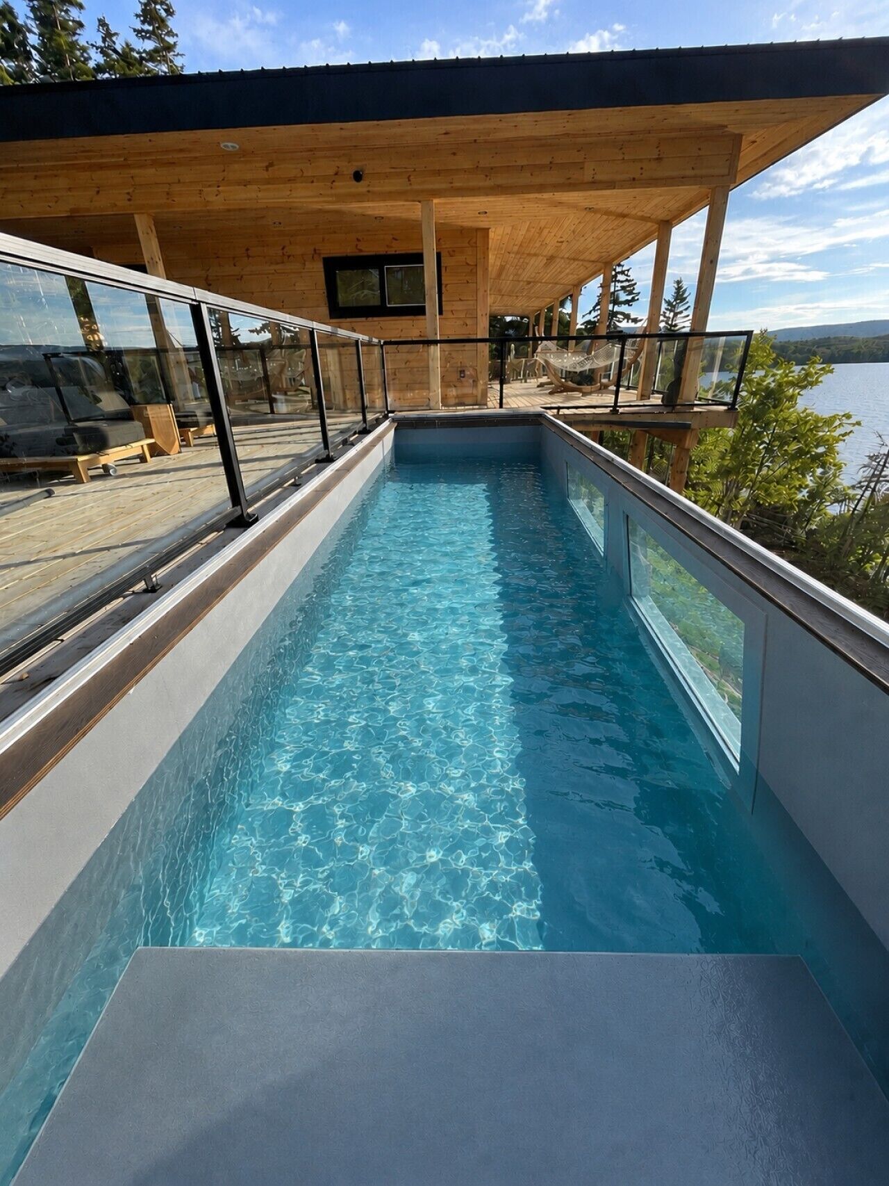 Ein moderner Außenpool mit Holzterrasse und Glasgeländern.