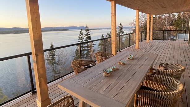 A wooden deck with a table and chairs, overlooking a body of water and trees.