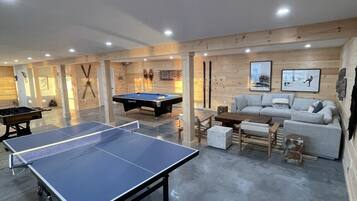 A room with a ping pong table, pool table, and a sofa.