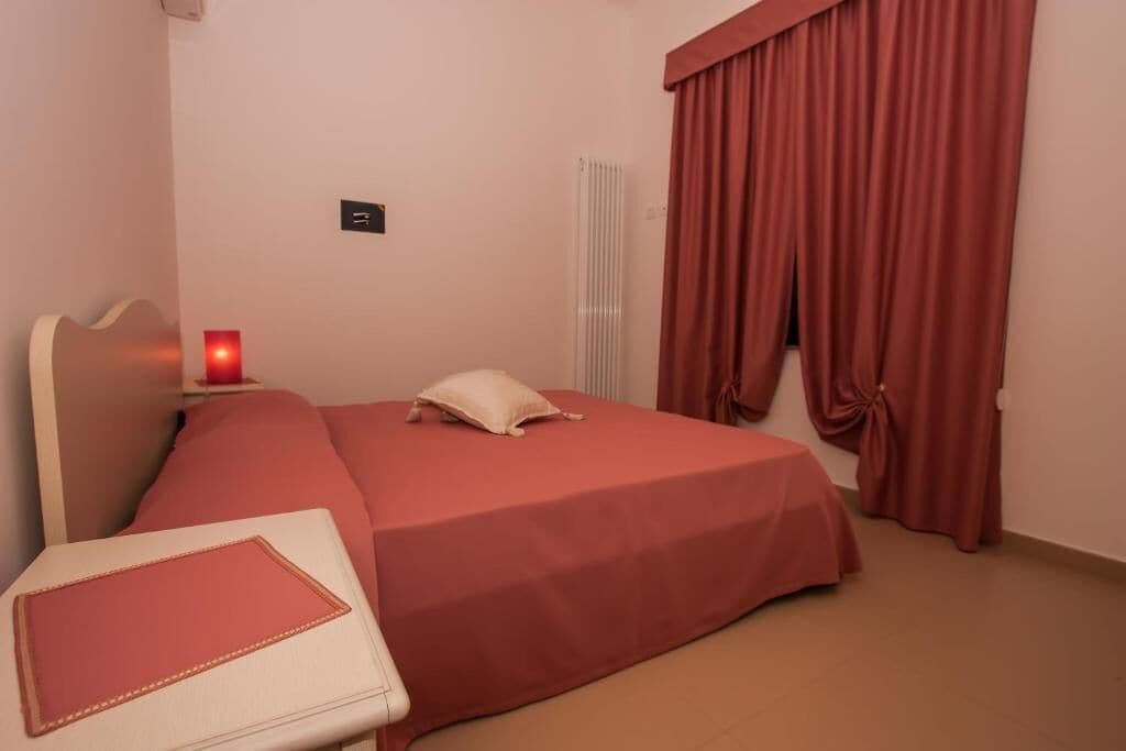 A hotel room with a bed, a bedside table, a lamp, and a window with curtains.