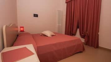 A hotel room with a bed, a bedside table, a lamp, and a window with curtains.