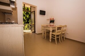 A kitchen with a gas stove, a dining table with chairs, a potted plant, and a TV on the wall.
