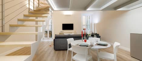 A modern interior with a dining area, a sofa, a TV, and a staircase.