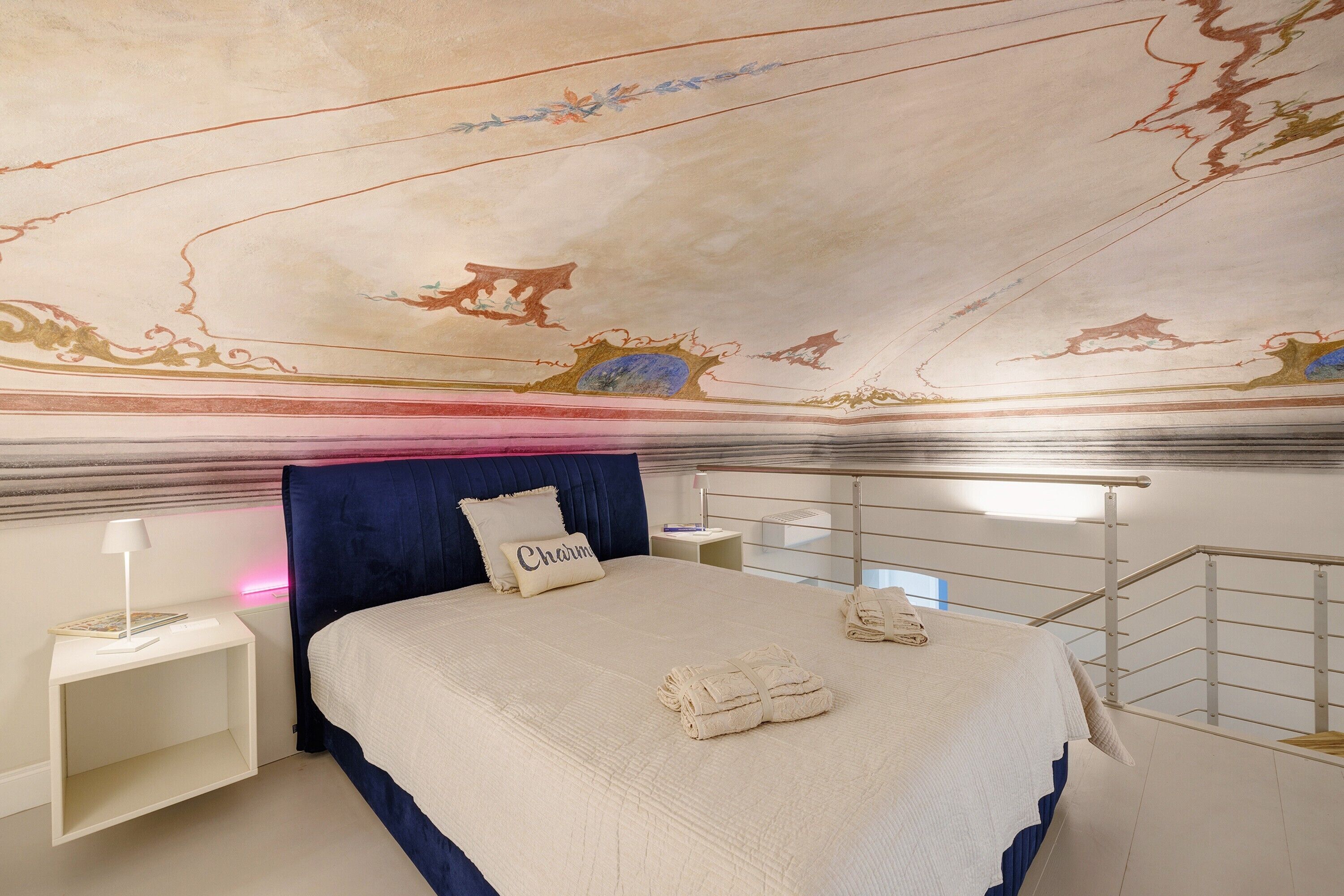 Une chambre à coucher avec un grand lit, une tête de lit, une table de chevet, une lampe et un plafond orné d’œuvres d’art décoratives.