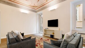 Una sala de estar moderna con dos sofás grises, un televisor de pantalla plana y un techo decorativo.