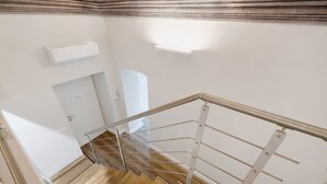 Una escalera con barandilla de metal, escalones de madera y una pared blanca con un termostato.