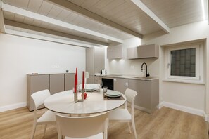 A modern kitchen with a dining area, featuring a round table, white chairs, and a window with a view.