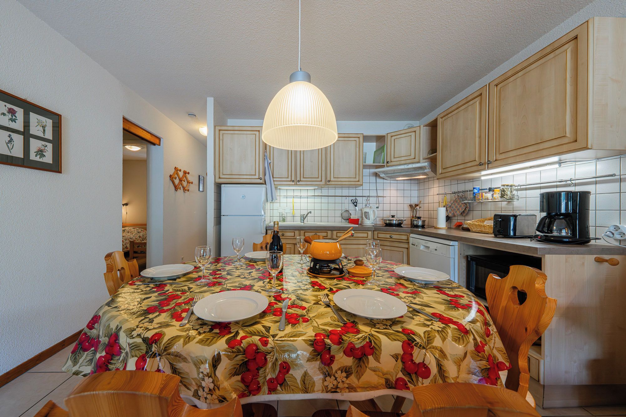 A dining area with a table set for four, surrounded by wooden chairs. There is a hanging light fixture above the table.