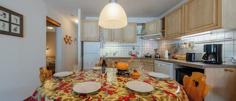 Un comedor con una mesa preparada para cuatro personas, rodeada de sillas de madera. Hay una lámpara colgante sobre la mesa.