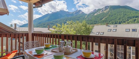 Un balcón con una mesa dispuesta para tomar té, con vistas a un paisaje montañoso.