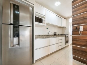 A modern kitchen with stainless steel appliances, white cabinetry, and a wooden accent wall. - Porto Fino by LikeHome  (Bombinhas)
