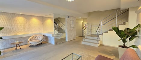 Un intérieur moderne avec une table basse en verre, un fauteuil en osier, un escalier et une plante en pot.