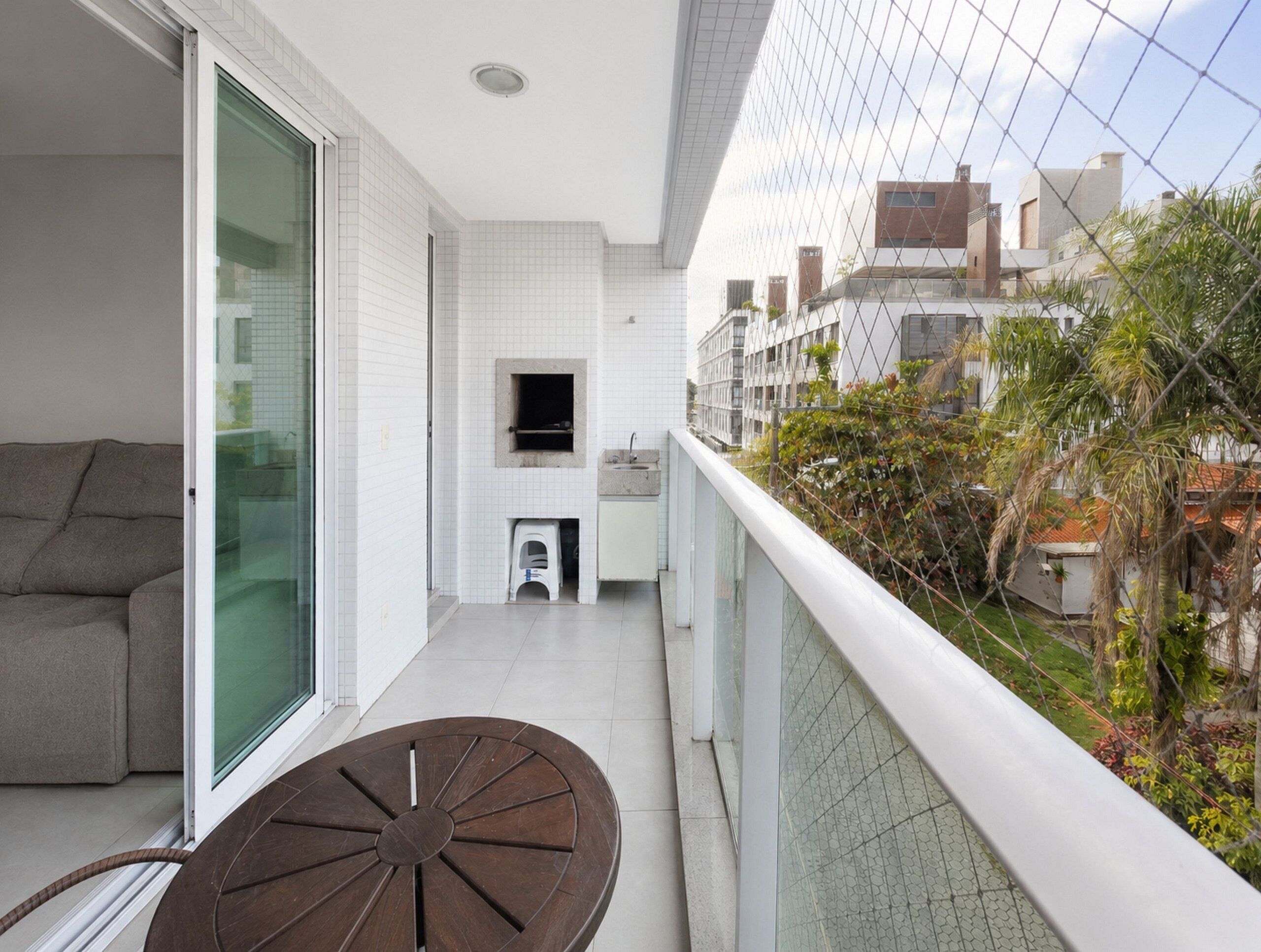 A balcony with a sofa, a table, and a view of buildings and greenery.